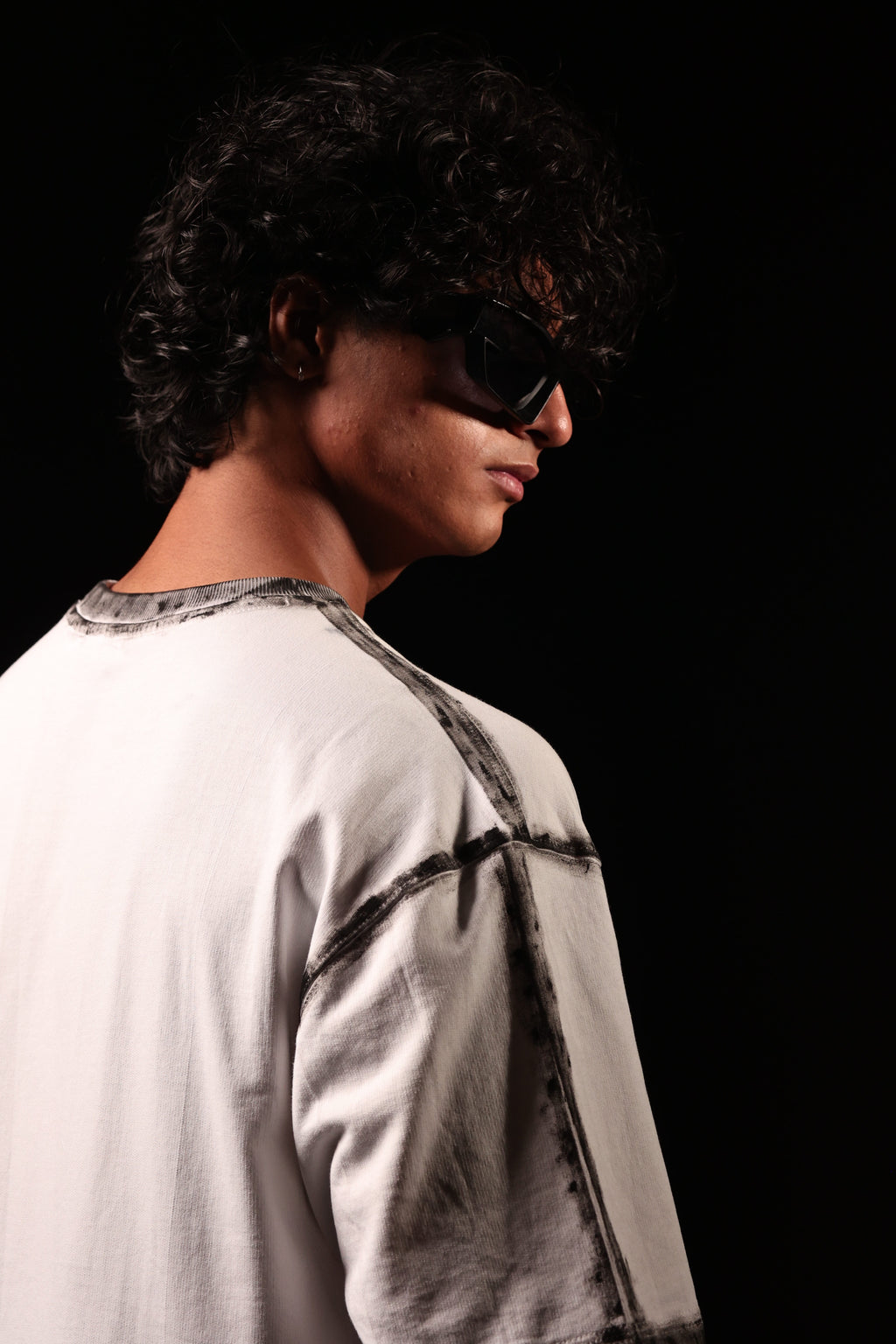 Person wearing sunglasses and a light-colored shirt against a black background