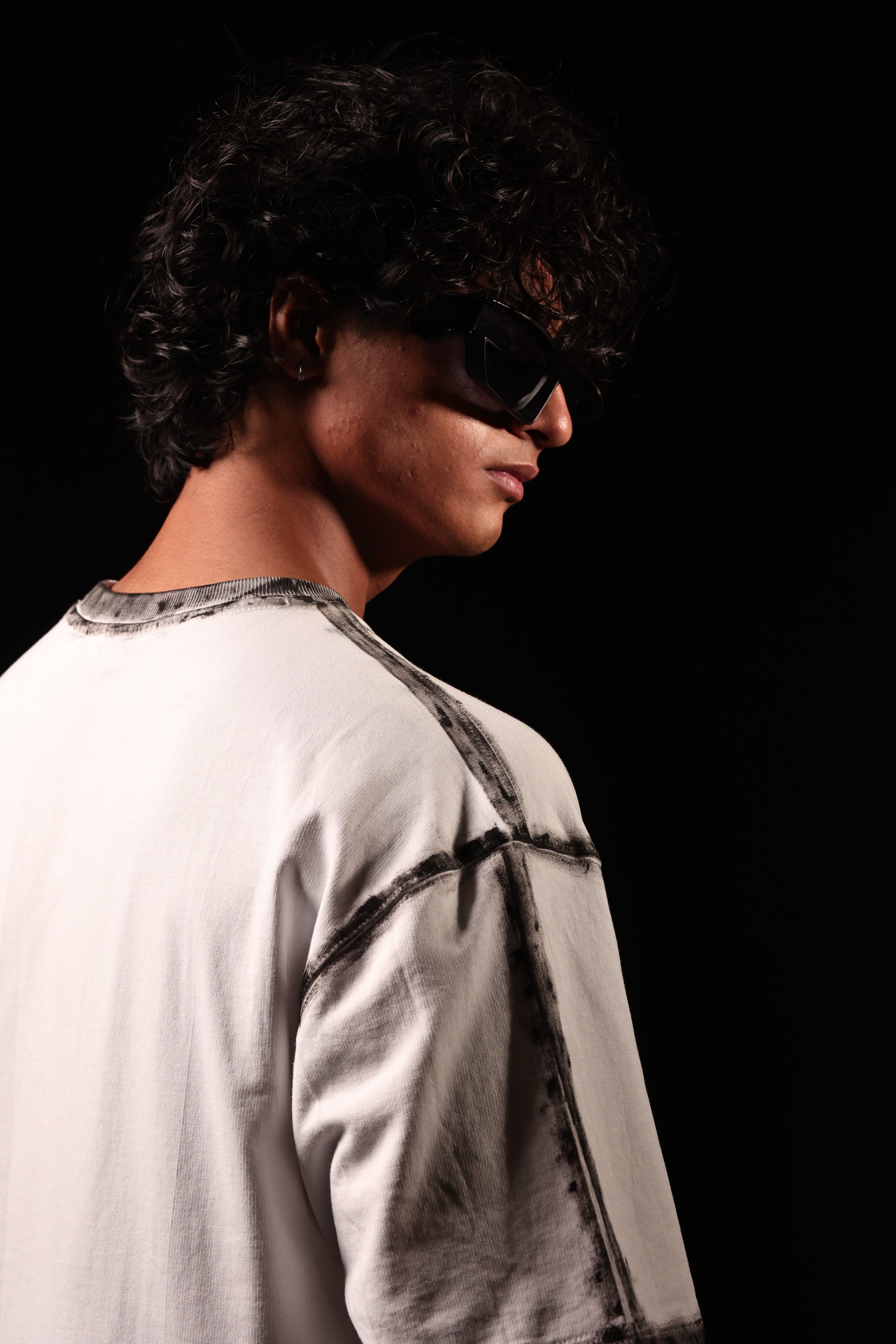 Person wearing sunglasses and a light-colored shirt against a black background