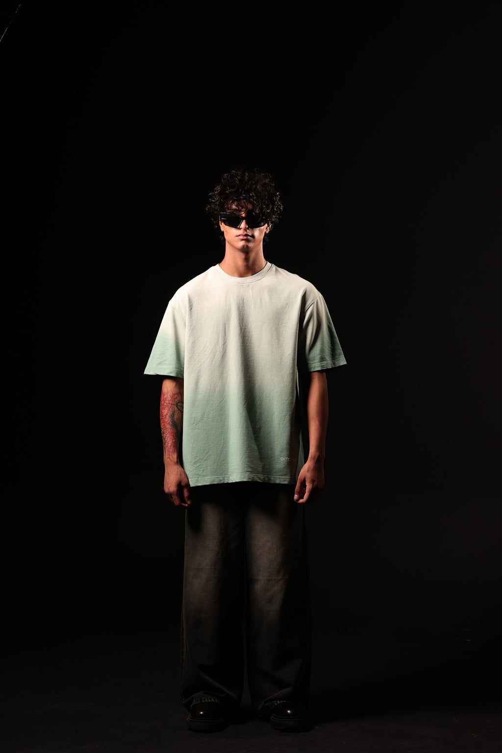 Person wearing a light green t-shirt and dark pants against a black background