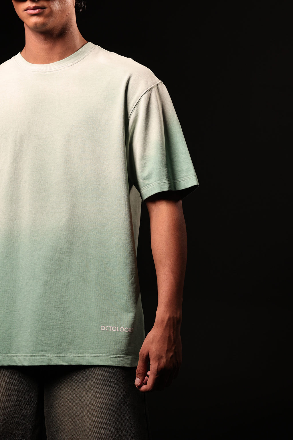 Person wearing a light green t-shirt with a brand logo on a black background