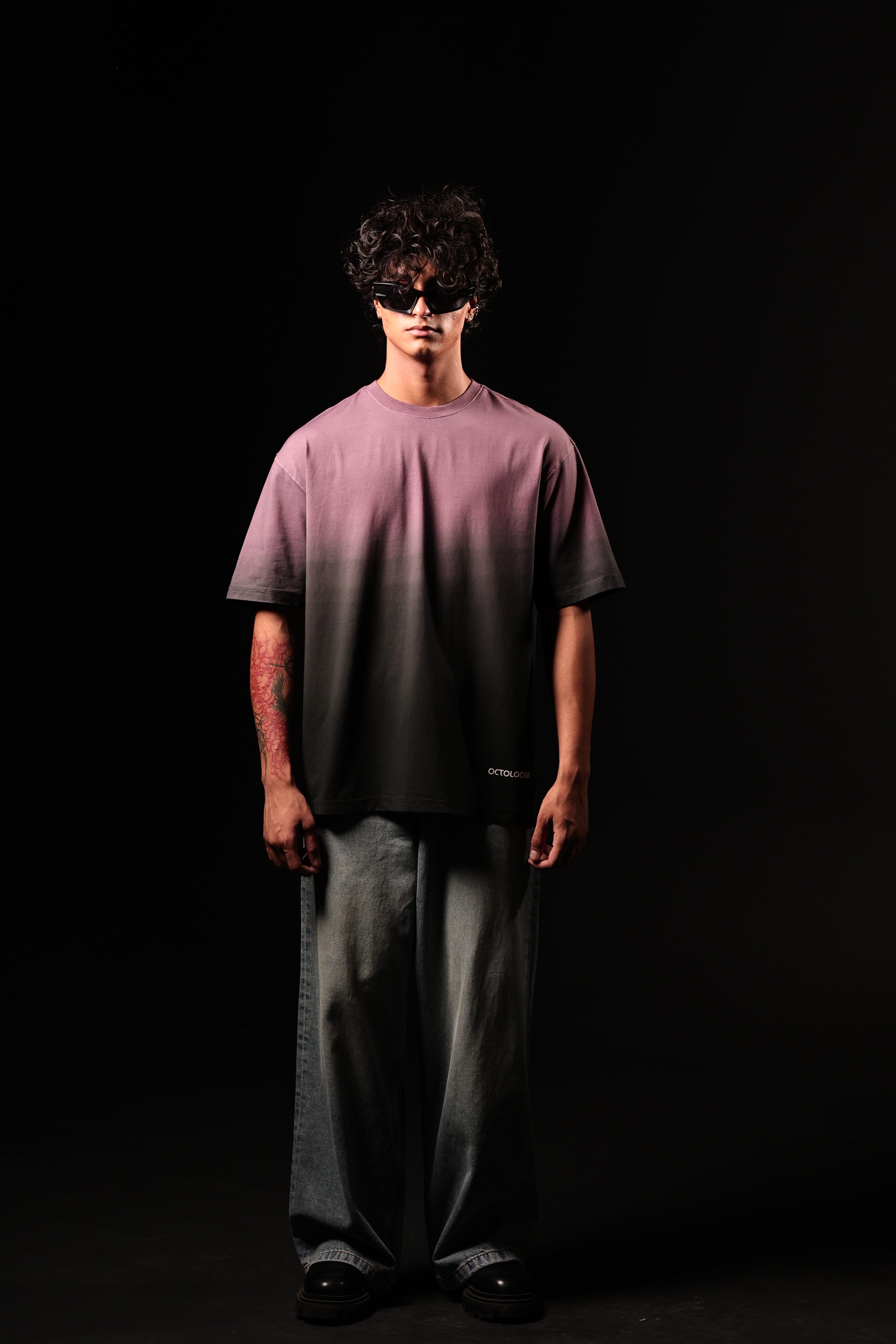 Person wearing a purple shirt and gray pants against a black background