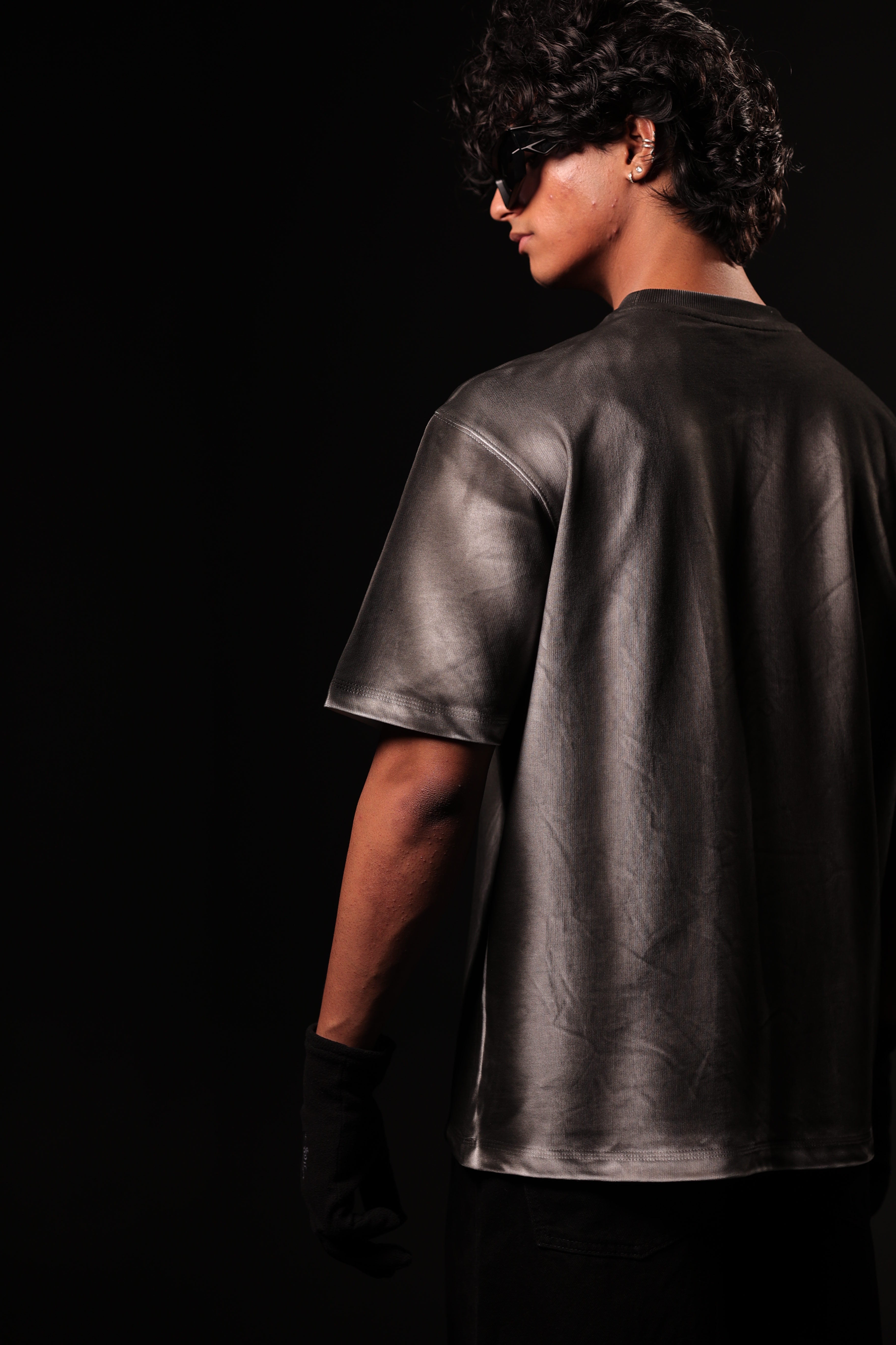 Person wearing a shiny black leather outfit against a dark background