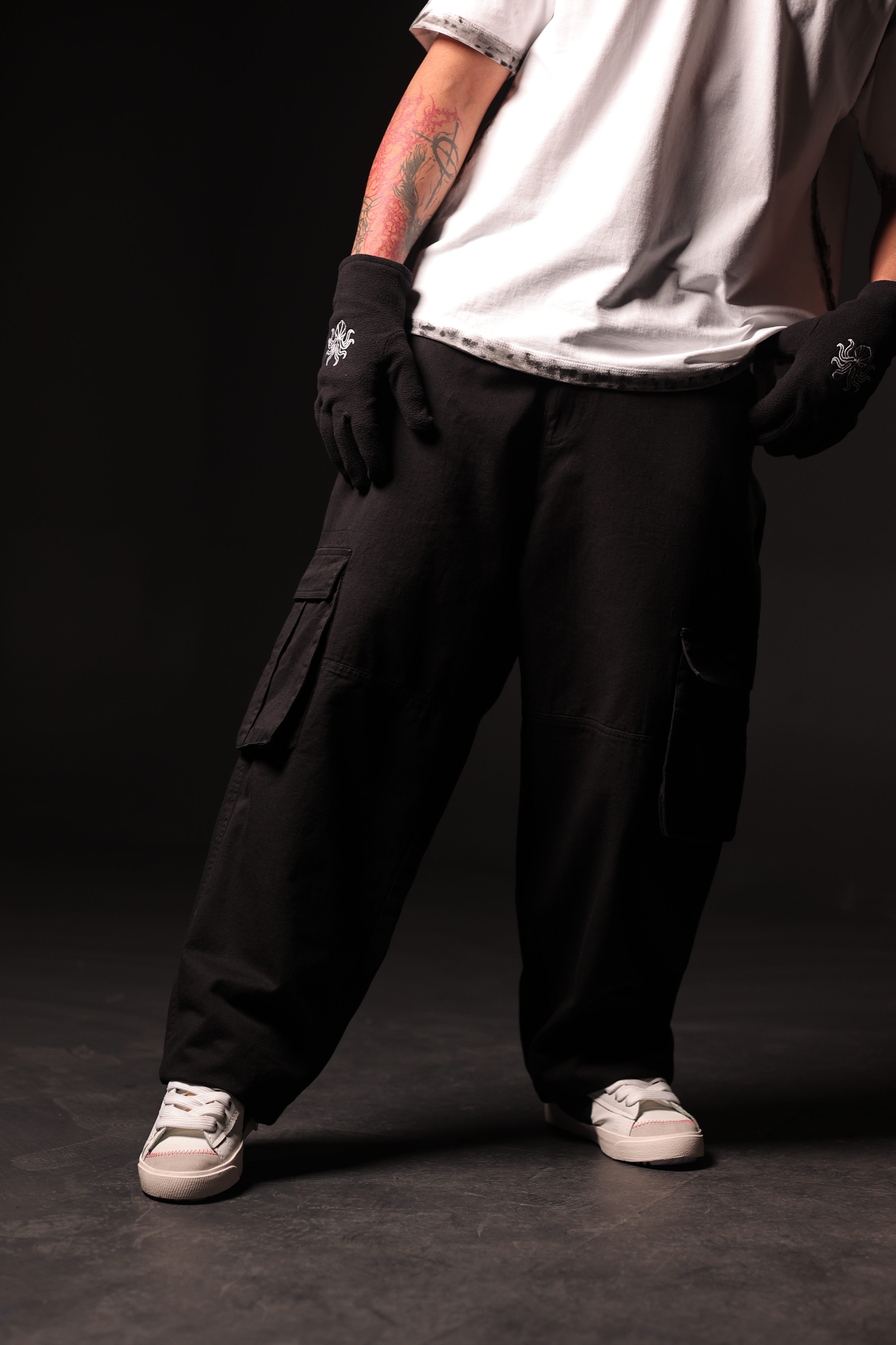 Person wearing black cargo pants and gloves on a dark background