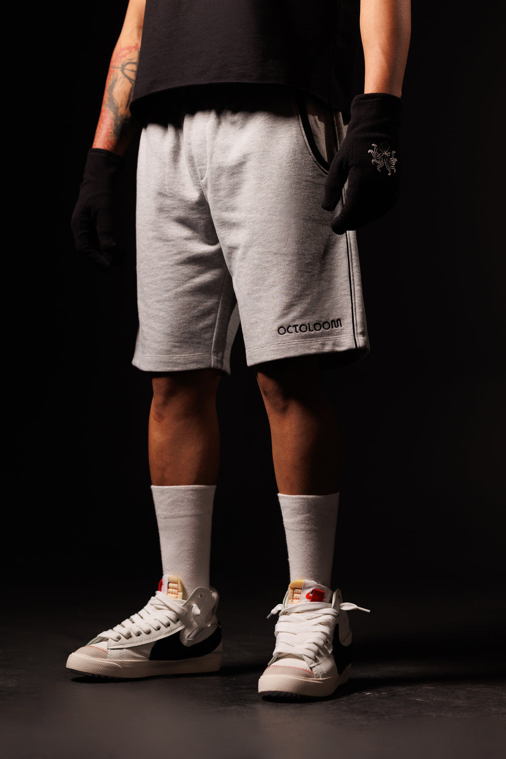Person wearing gray shorts with a brand logo, white sneakers, and white socks on a black background