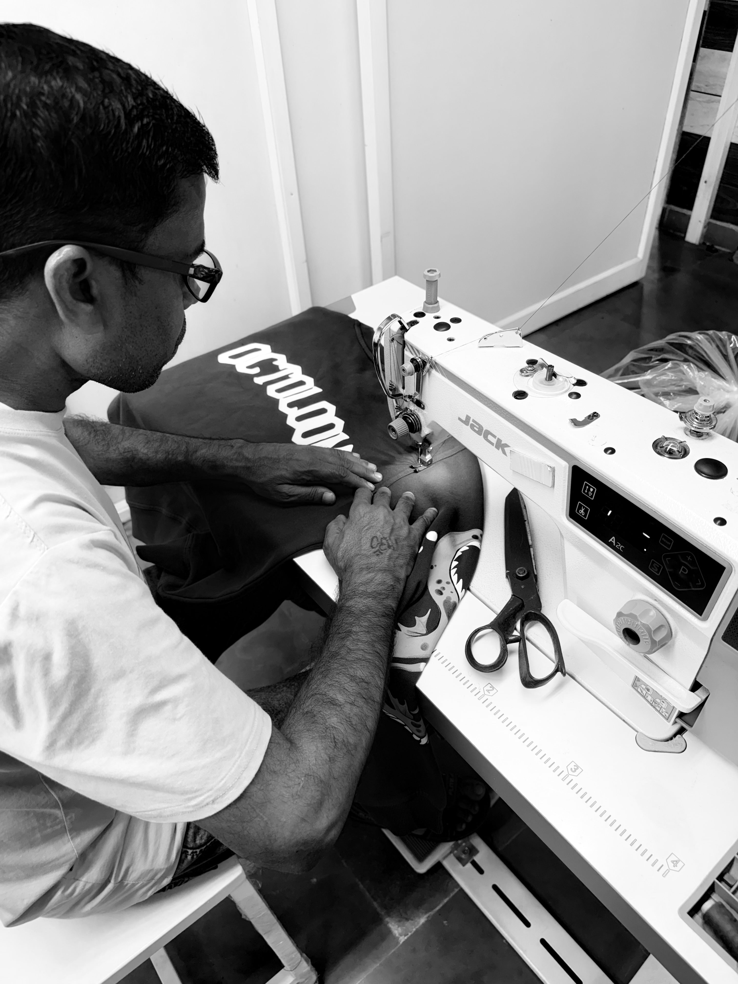 Person working on a sewing machine with a shirt on a table.