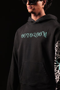 Person wearing a black hoodie with 'OCTOLOOM' text and a colorful sleeve design on a dark background