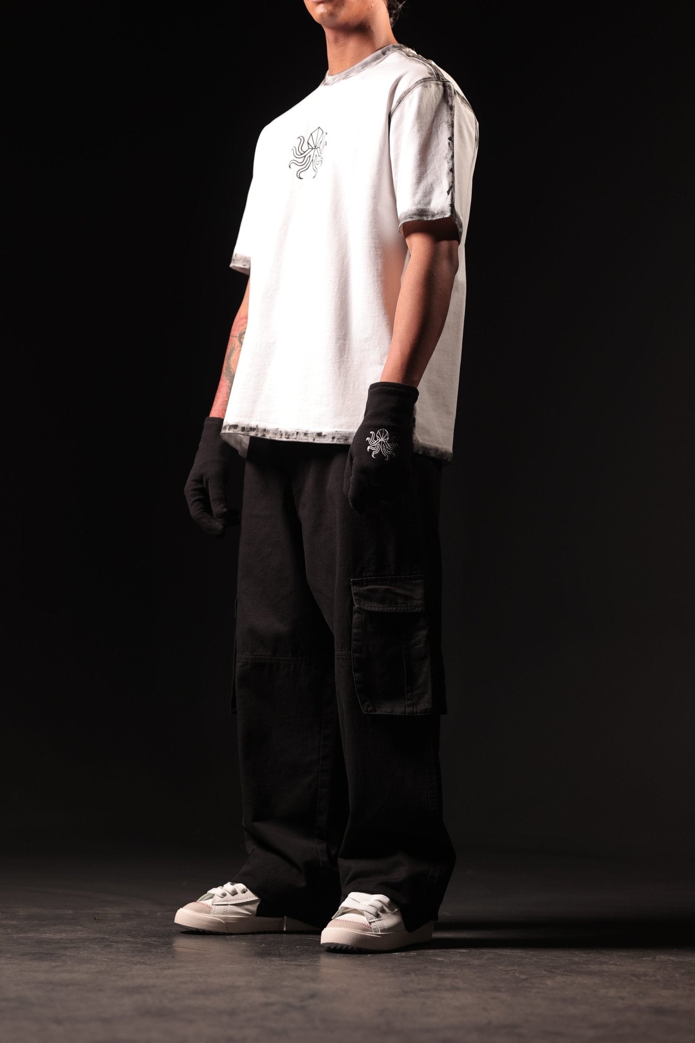 Person wearing a white t-shirt, black gloves, and dark pants on a black background
