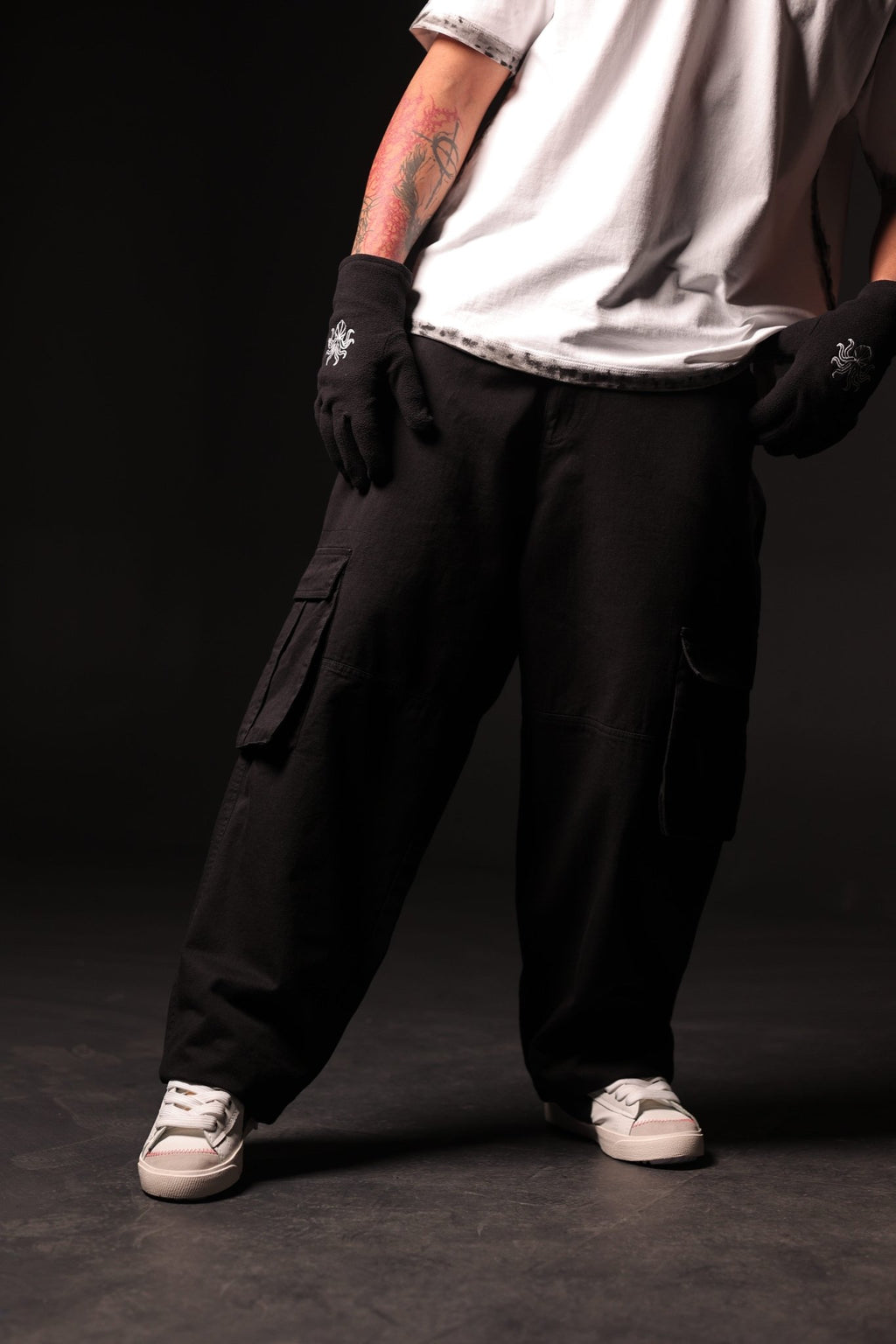 Person wearing black cargo pants and gloves on a dark background