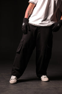 Person wearing black cargo pants and gloves on a dark background