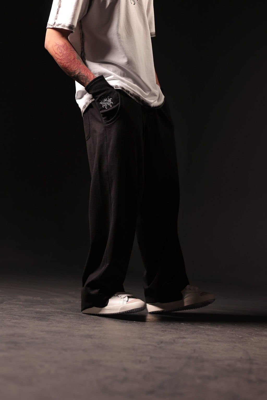 Person wearing a light-colored shirt, dark pants, and white shoes on a black background