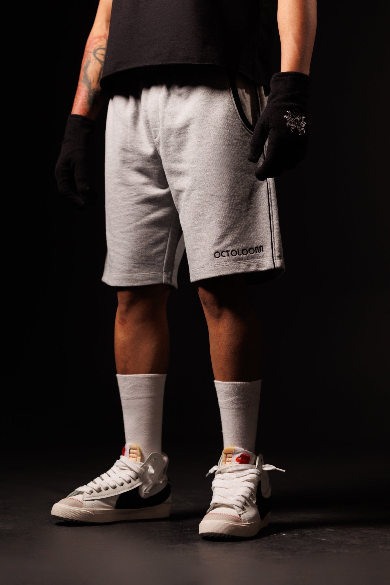 Person wearing gray shorts with a brand logo, white sneakers, and white socks on a black background
