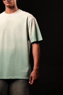 Person wearing a light green t-shirt with a brand logo on a black background