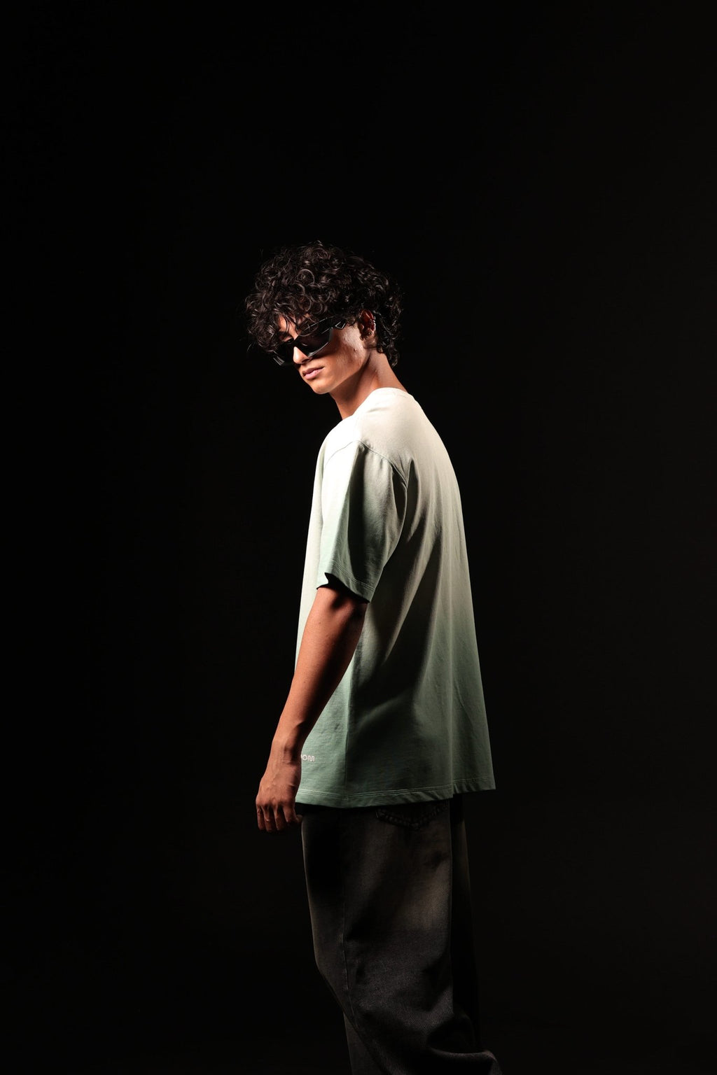 Person wearing a light green t-shirt and dark pants against a black background
