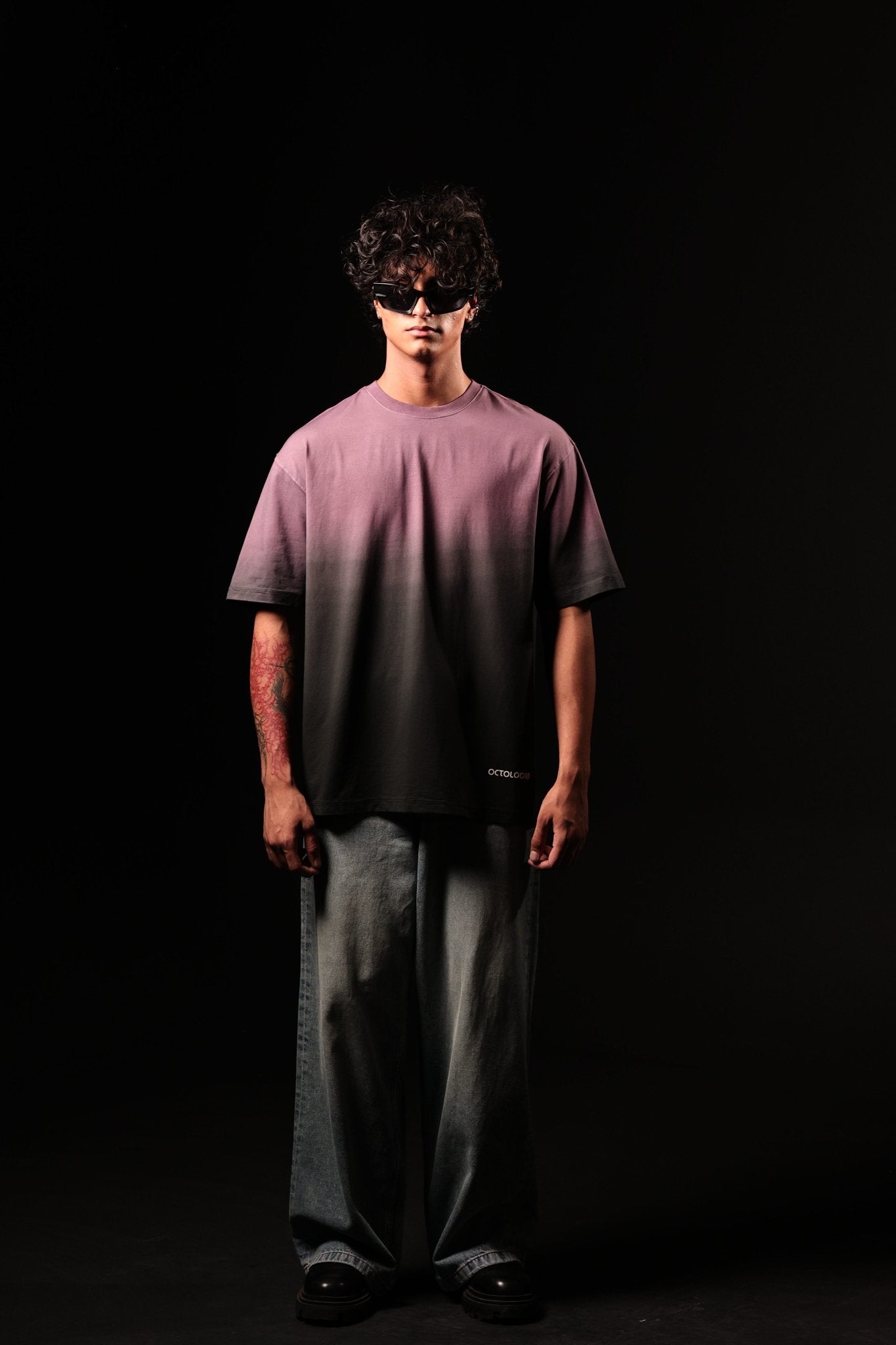 Person wearing a purple shirt and gray pants against a black background